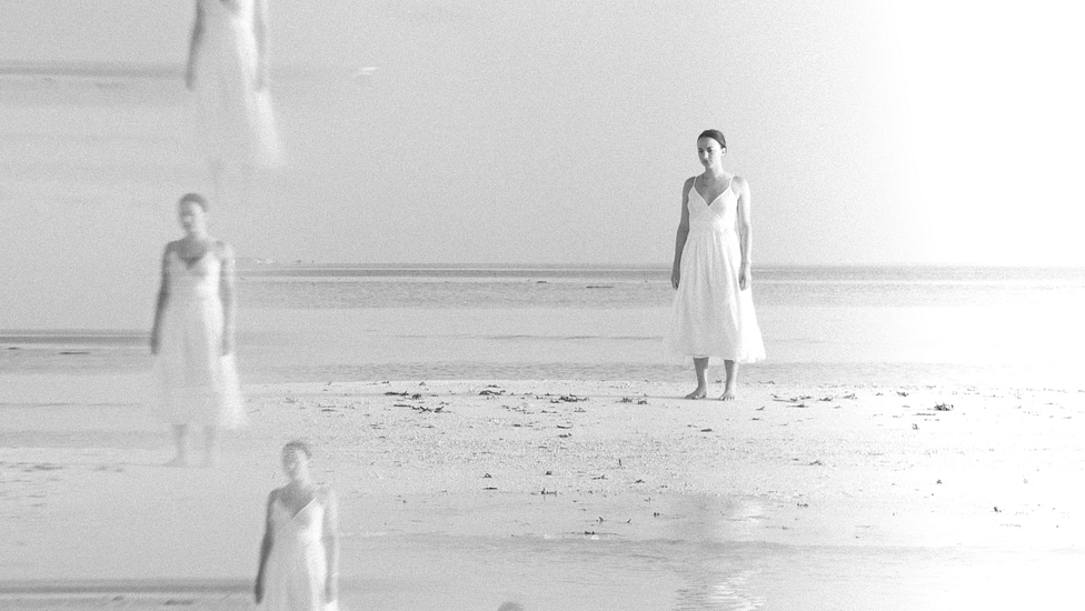 poems about strength - a multi-exposure photo in grayscale, a woman standing on a beach in a white dress.