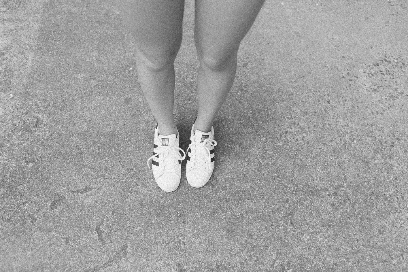 A greyscale image of a pair of legs in trainers